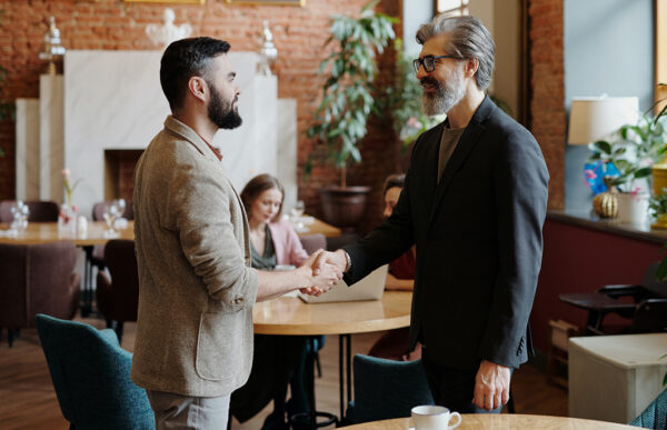 Two people with beards and blazers shaking hands in office.