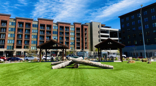 Apartment dog park with lush grass, climbing logs, and gazebos.