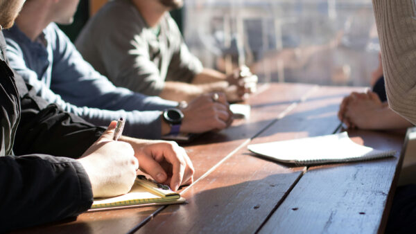 Co-workers collaborating at a wood table with notepads.
